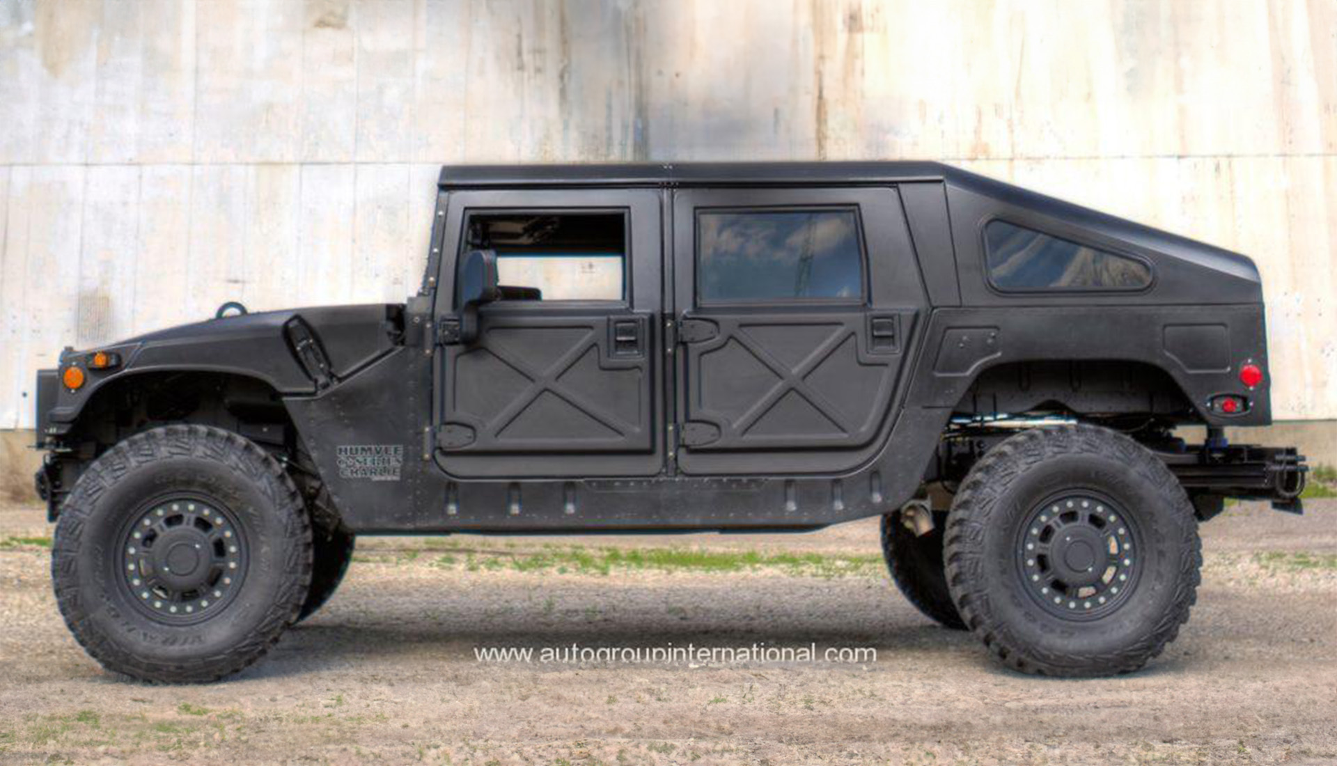 Black armored Humvee vehicle parked against concrete wall.