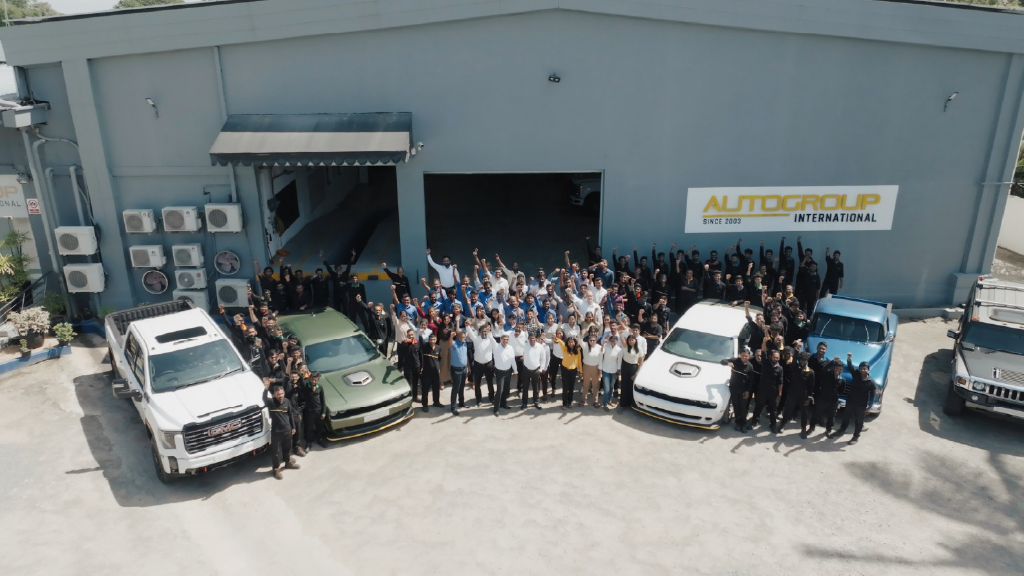 Team celebrates with trucks at AutoGroup International's garage.