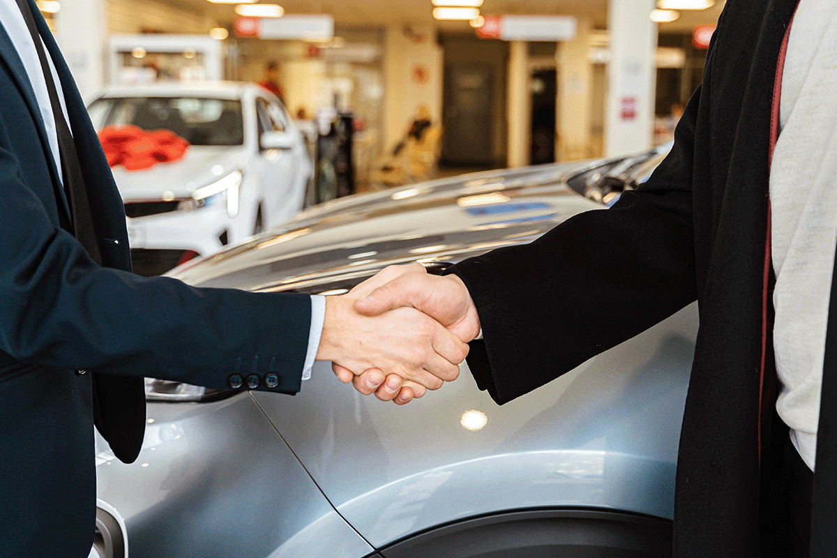 Two people shaking hands over car in dealership.