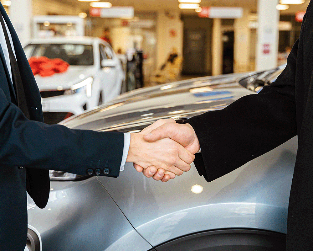 two people shaking hands near a vehicle in background